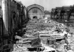 Blick auf die Trümmer des ehemaligen Querbahnsteigs des Leipziger Hauptbahnhofs. Der Angriff der 8. US-Luftflotte am 7. Juli 1944 verursachte schwerste Beschädigungen vor allem an der Westhalle und der Querbahnsteighalle. 46,2 Tonnen Bomben trafen an diesem Tag den Bahnhof, wobei zunächst einer der stützenden Abschlussbögen aus Stahlbeton brach. Dadurch kam es in den folgenden 20 Minuten zu einer Kettenreaktion, bei der die Stahlbetonbögen zwischen den Hallenschiffen und das Dach der Querbahnsteighalle komplett einstürzten. Die Osthalle blieb weitgehend unversehrt. An diesem Tag starben in den Luftschutzkellern zwischen den Bahnsteigen hunderte Eisenbahner und Reisende. Unmittelbar vor dem Hauptbahnhof und in der klaffenden Lücke des zerstörten Querbahnsteigs auf der Ebene der einstigen Gepäckanlagen mussten innerhalb von sechs Jahren rund 20.000 Sprengungen ausgeführt und 30.000 Kubikmeter Schutt beseitigt werden. Die Sprengungen waren nötig, um die Stahlbetontrümmer so weit zu verkleinern, dass sie abtransportiert werden konnten. Ab 19.07.1945 konnte Leipzig Hbf wieder elektrisch befahren werden (bis zur sowjetischen Demontage im März 1946). Zur ersten Messe im März 1946 waren einige Bahnsteige wieder komplett betretbar und 1947 anlässlich der Frühjahrsmesse war der Querbahnsteig wieder teilweise nutzbar. 1948 folgten die wichtigsten Ausbesserungen am Querbahnsteig. Zur Herbstmesse waren 7.000 Quadratmeter wiederhergestellt. 1949 war die Osthalle im Wesentlichen wiederhergestellt. Im Jahr darauf erreichte die neu gezogene Betondecke in der Querbahnsteighalle 9.000 Quadratmeter. (1947) <i>Foto: Historische Sammlung der Deutschen Bahn AG</i>